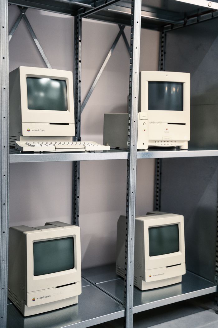 Collection of vintage Apple computers displayed on metal shelving indoors.
